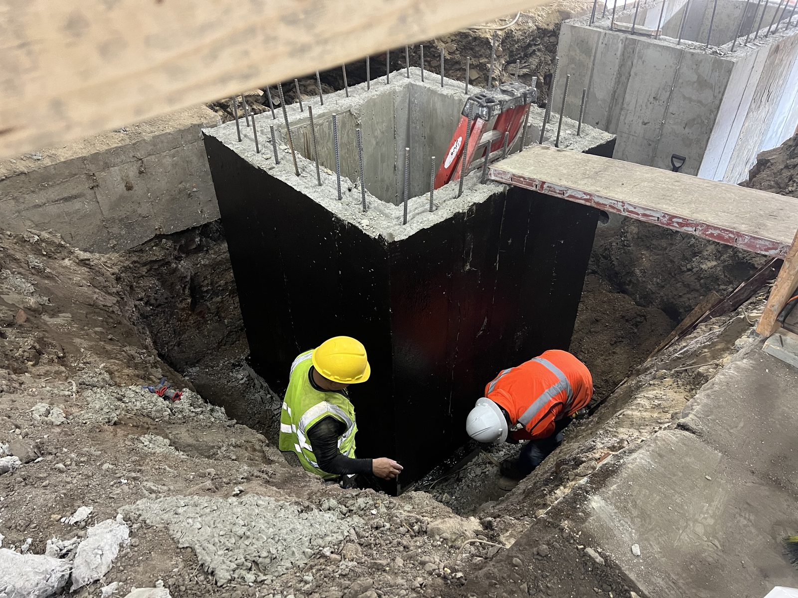 JBS foundation underpinning with waterproofed concrete pier and rebar dowels, workers in PPE