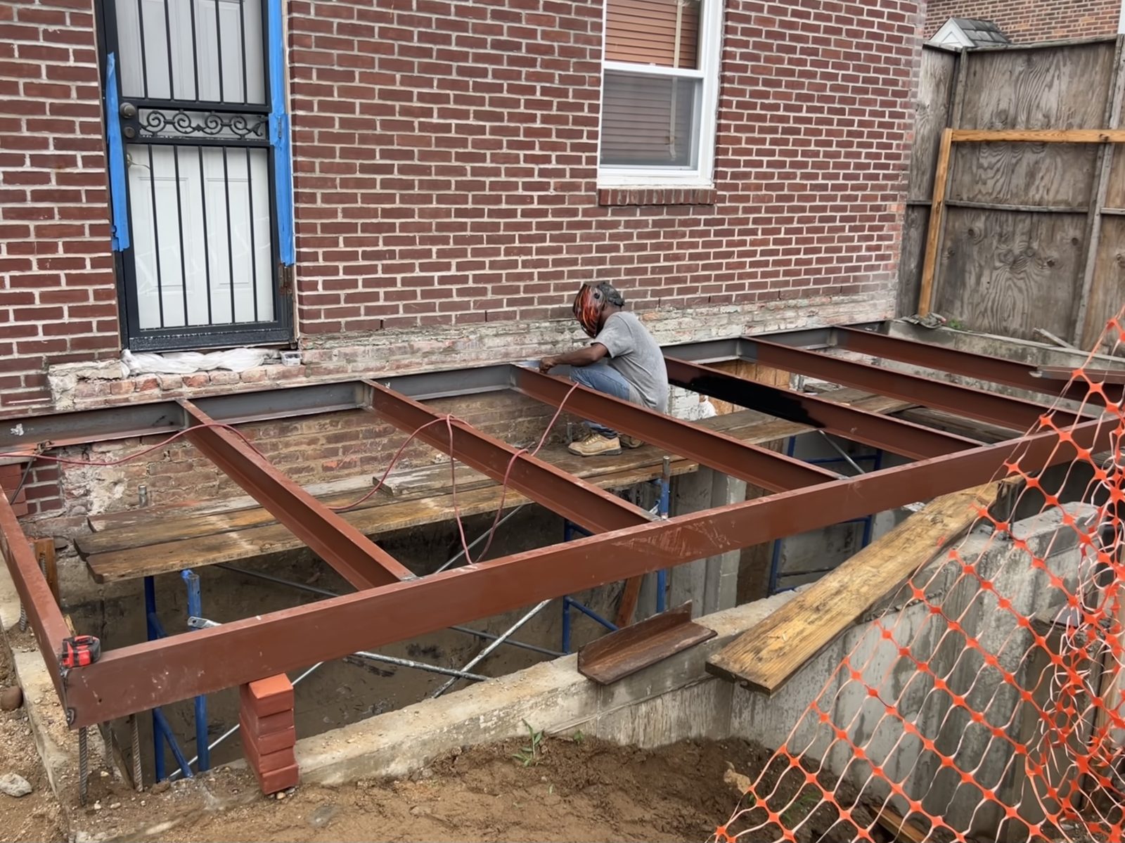 JBS NYC steel I-beam framing for residential rear extension with welder on site