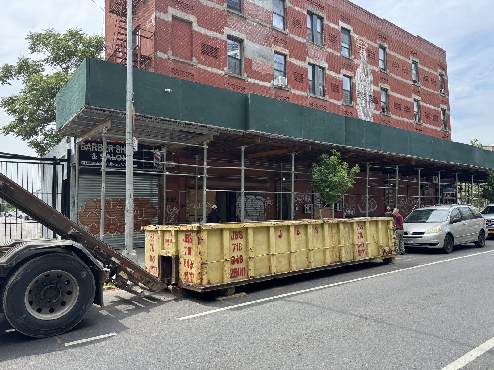 JBS 30 yard dumpster on roll-off truck at Brooklyn job site with scaffolding